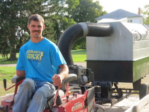 Lawn care professional with one functional arm driving a zero-turn mower onto a trailer.