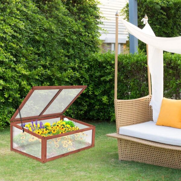 Portable cold frame with flowers inside and a lid lifted up that's set outside in an outside patio area.