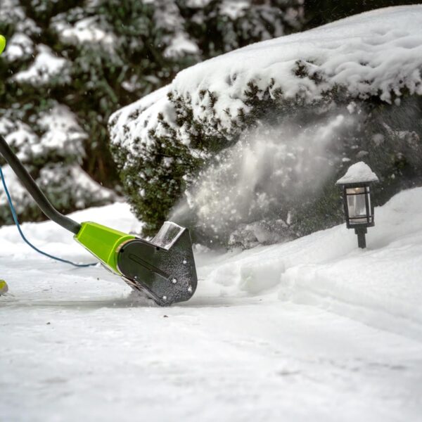 Someone using an electric snow shovel to clear a driveway.