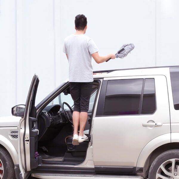 A guy has one foot on the door latch step to be able to wash the top of his car.