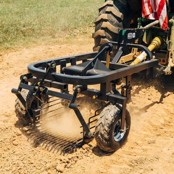 A tractor has a PTO powered potato digger attached to the back while driving down a field digging up the ground.