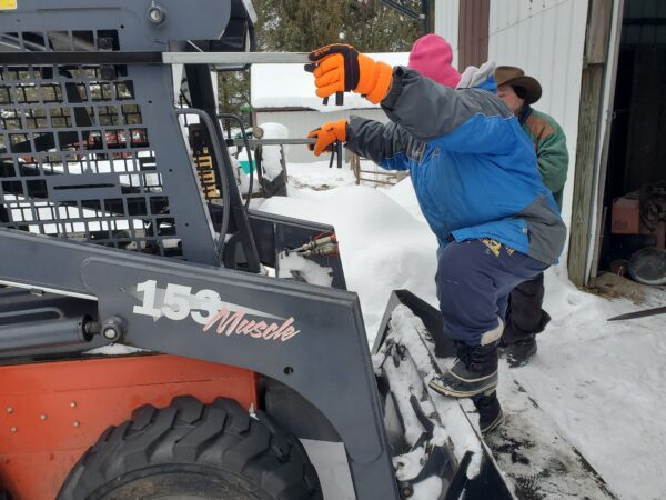 A person climbing onto a skid steer using a loader bucket step