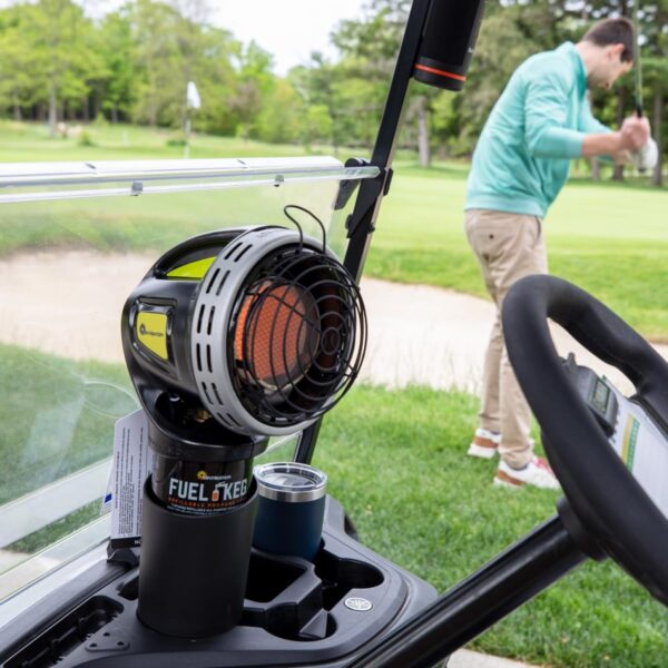 The heater sitting in a golf cart while someone is swinging a golf club in the background.